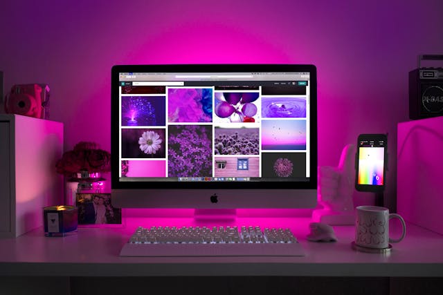 Desktop iMac displaying a grid of colorful photos on a pink-lit desk